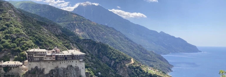 Kloster auf einem Felsen mit Berglandschaft und Meer im Hintergrund.