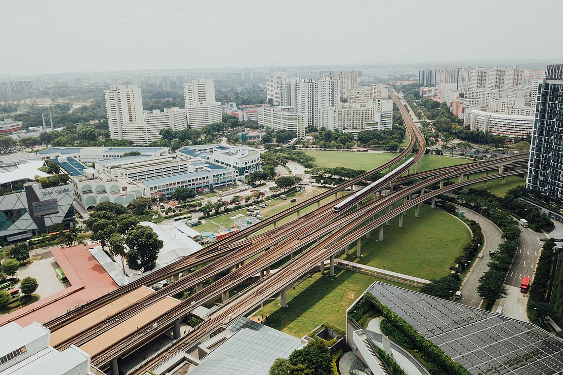 Luftaufnahme einer Stadt mit mehrspuriger Autobahn, Wohngebäuden und Grünflächen.
