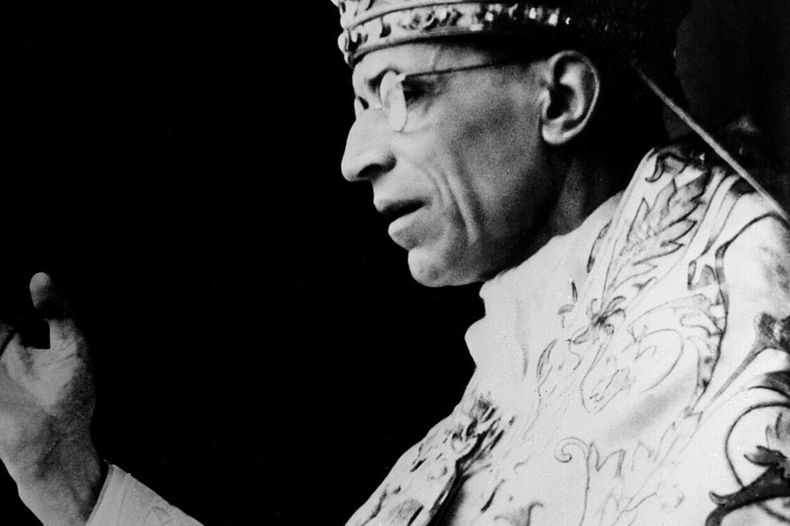Schwarz-weiß-Fotografie von Pius XII in liturgischer Kleidung mit erhobener Hand.